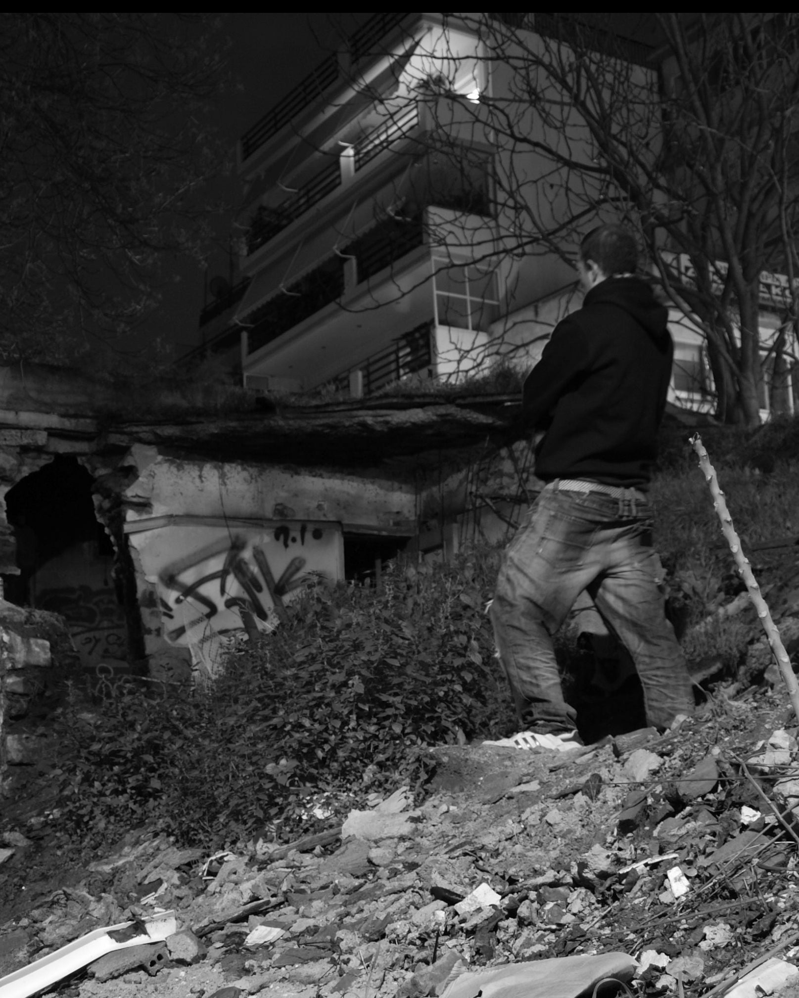 Spam looking at one of his ASK tags through a desolate urban area with debris and dilapidated buildings at night.